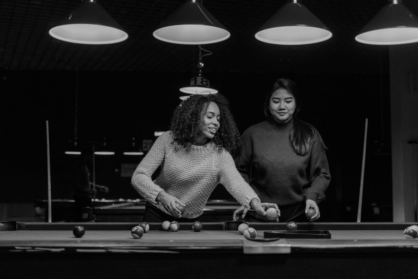 Two women playing billiards in a modern nightclub setting, enjoying leisure time.