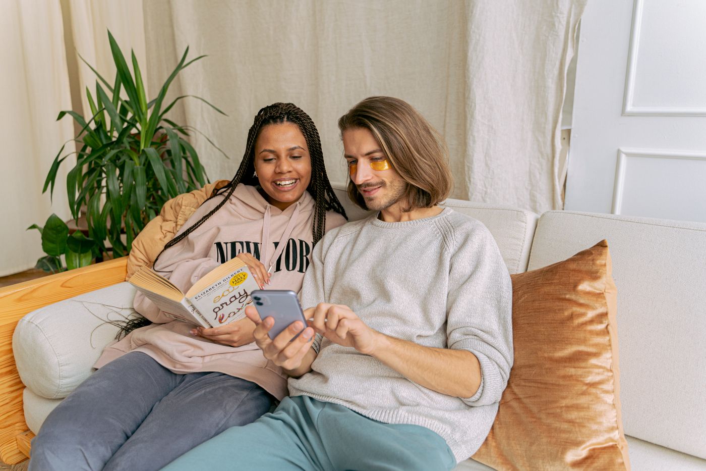 A happy couple relaxing on the sofa, reading and using a smartphone indoors.